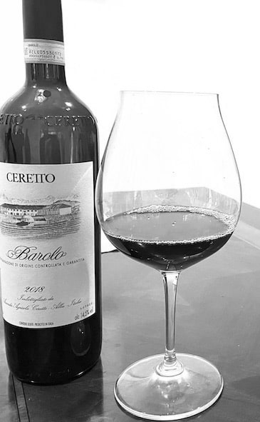 A bottle of Barolo wine next to a glass of the wine on a table
