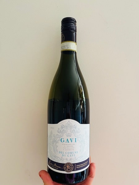 A hand holding a bottle of Gavi di Gavi wine against a wall