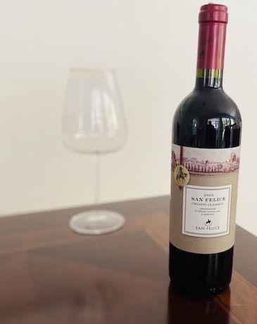 A bottle of red chianti classico wine on a wood table with a wine glass in the background