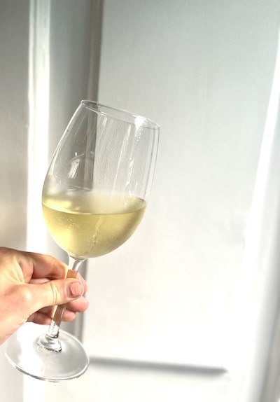 Hand holding a glass of white wine against a white kitchen cabinet background