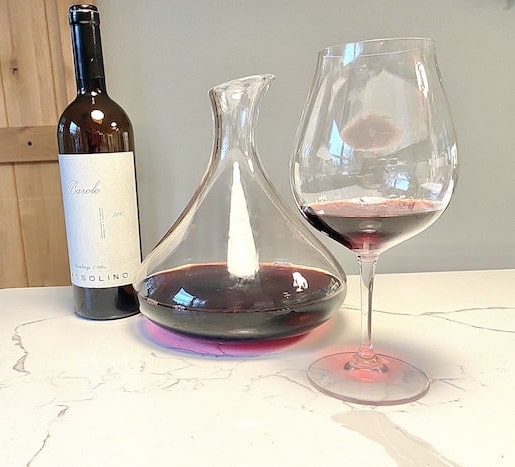 Bottle of Barolo, decanter and Barolo Barbaresco wine glass on a white countertop with a wood and wall background