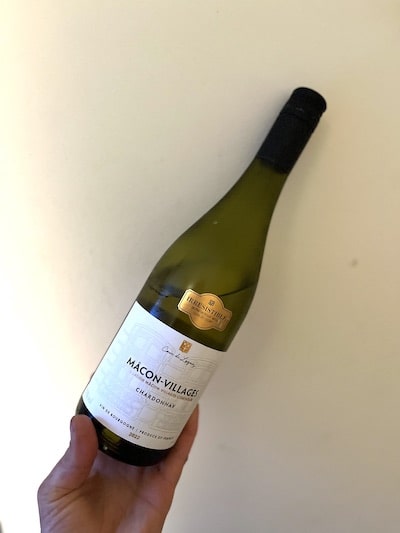 A hand holds a bottle of French Chardonnay Mâcon-Villages vertically against a white background