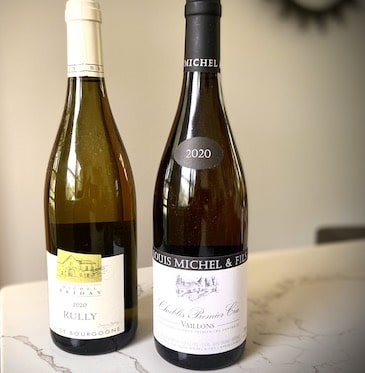 Two bottles of white French Chardonnay on a marble countertop with a plain background